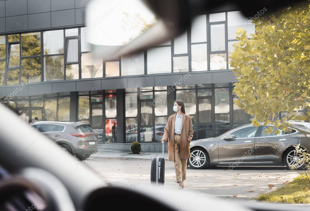 elegante donna in abito autunnale passeggiando lungo il parcheggio auto con valigia in primo piano sfocata
