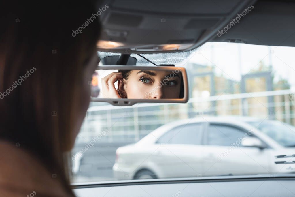 donna che fissa i capelli guardando nello specchio retrovisore dell'auto in primo piano sfocato