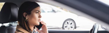 side view of young woman talking on smartphone while driving car on blurred foreground clipart