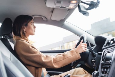 side view of woman in trench coat driving car on blurred foreground clipart