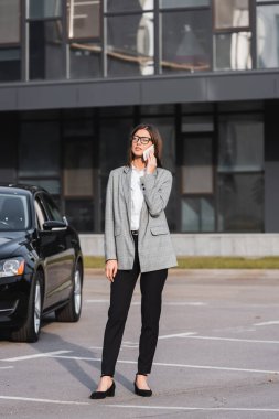 Siyah arabanın yanında akıllı telefondan konuşan şık bir iş kadını. 