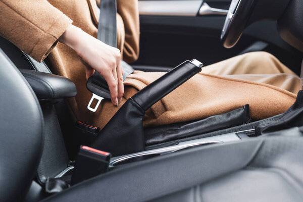 cropped view of woman fastening safety belt while sitting in car on blurred foreground