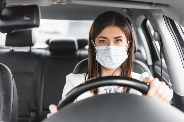 Kobieta Masce Medycznej Patrząc Przed Kamerą Podczas Jazdy Samochodem Niewyraźnym — Zdjęcie stockowe