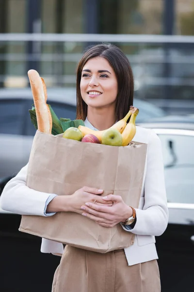 食料品をアウトドアで買い物袋を持ちながら見ている笑顔の女性 — ストック写真