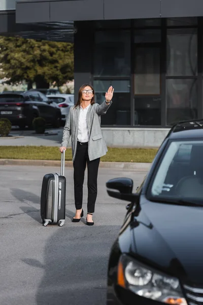 Stylish Businesswoman Suitcase Waving Hand Black Car Blurred Foreground — Stock Photo, Image