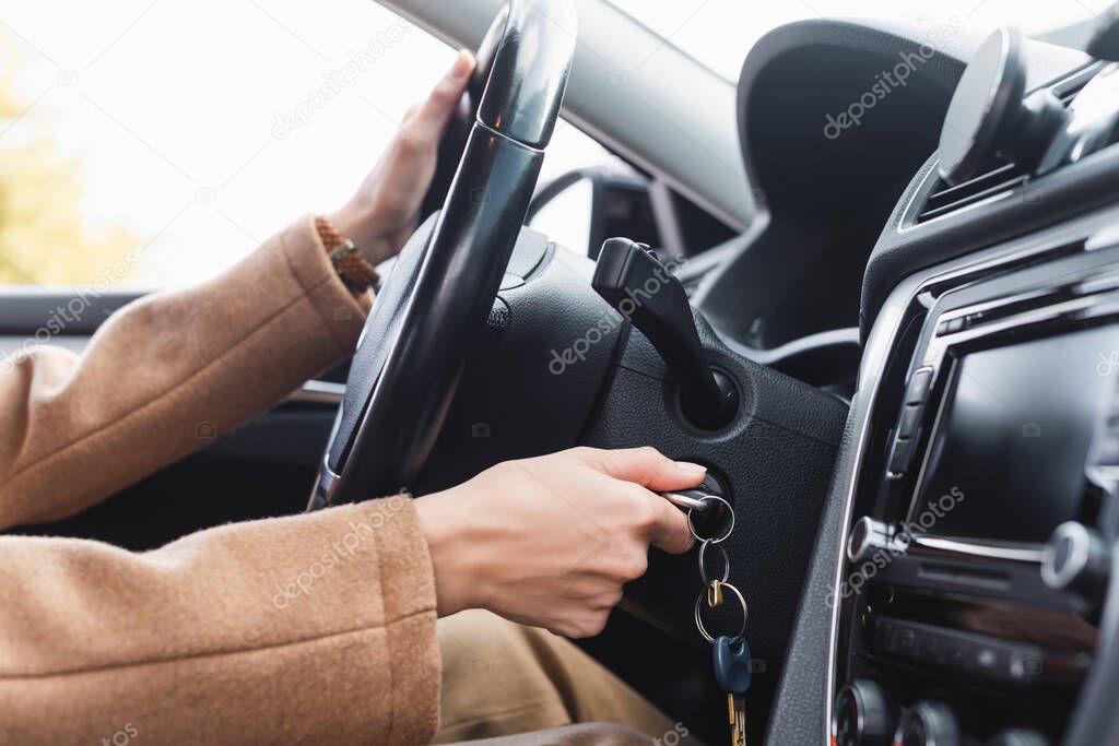 partial view of woman starting car while holding steering wheel