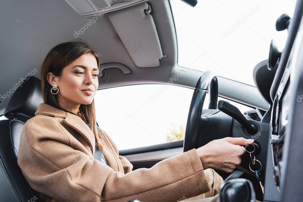 smiling woman in stylish trench coat starting car on blurred foreground