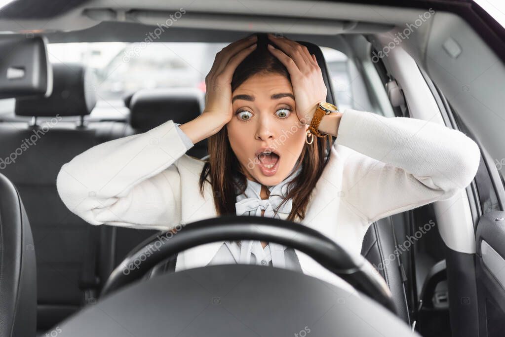 scared woman holding hands on head while sitting in car and looking at steering wheel