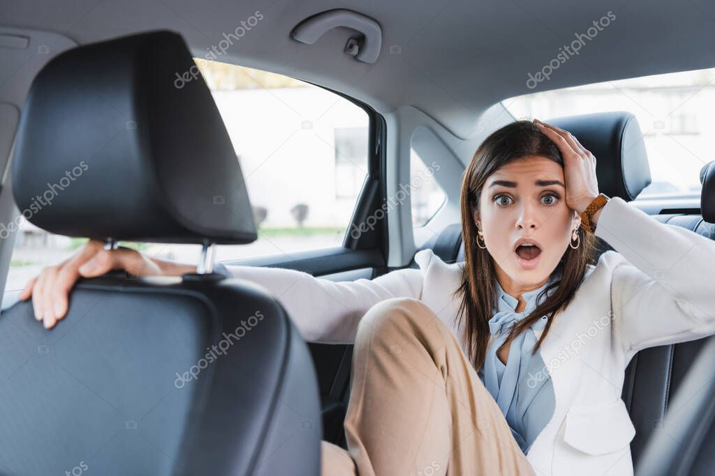 scared woman holding hand on head while riding in car on blurred foreground