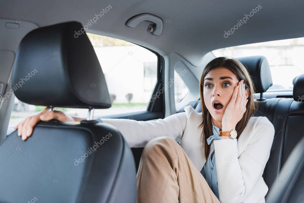 scared woman holding hand on face while sitting on back seat of car on blurred foreground