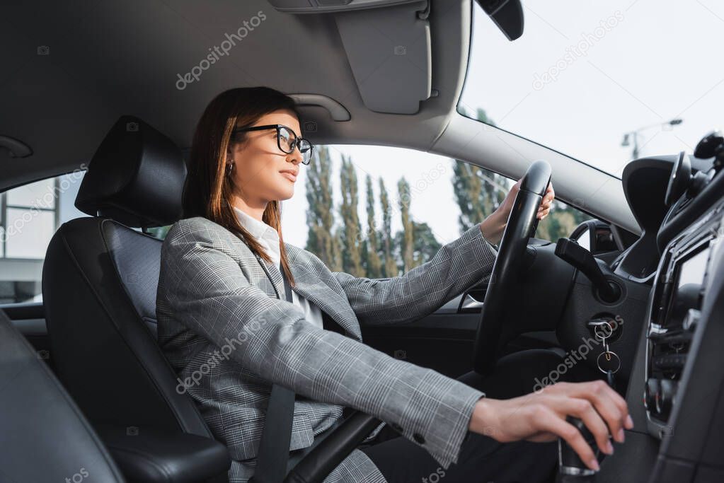 stylish businesswoman in eyeglasses shifting transmission lever while driving car