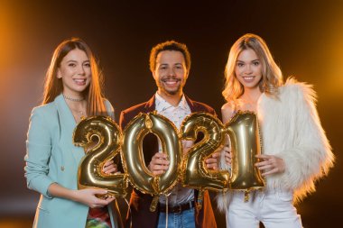 Afro-Amerikan bir adamla gülümseyen neşeli kadınlar ve elinde siyah üzerinde 2021 numara balonlar var. 