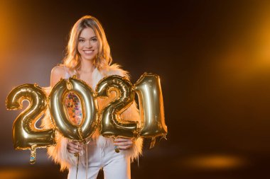 Gülümseyen ve elinde siyah üzerinde 2021 numara balonlar tutan neşeli sarışın kadın. 