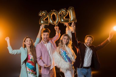 Bir grup heyecanlı çok kültürlü arkadaş ellerinde siyah üzerinde 2021 numara balon tutuyorlar. 