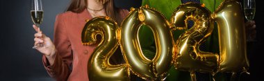 2021 numaralı balonları tutan çiftin kısmi görüntüsü ve siyah üzerine şampanya bardakları. 