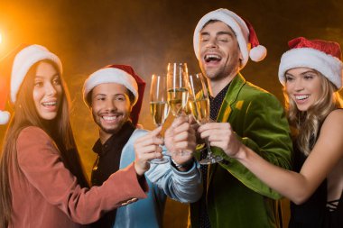 Noel Baba şapkalı mutlu çok kültürlü arkadaşlar. Siyah bardakta şampanya tokuşturuyorlar. 