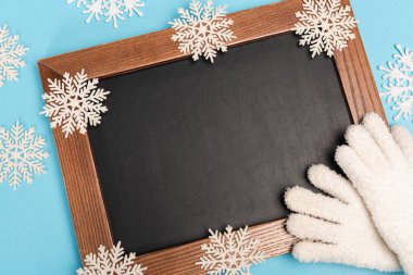 Kış manzarası beyaz eldivenler, karatahta ve mavi arka planda kar taneleri