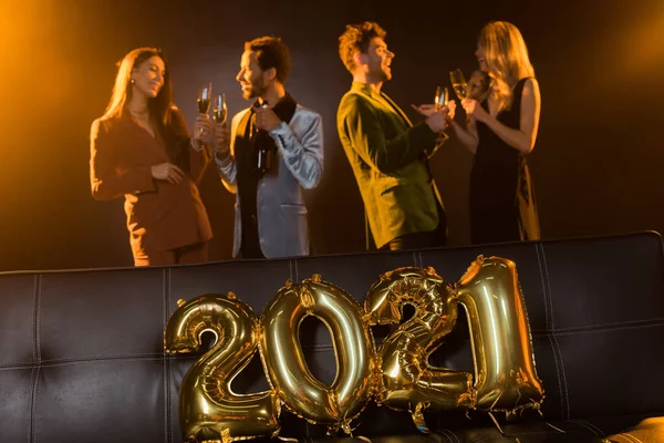 由快乐的多文化朋友们拼凑在沙发边 在黑色背景的2021年气球上 用香槟敬酒敬酒 — 图库照片