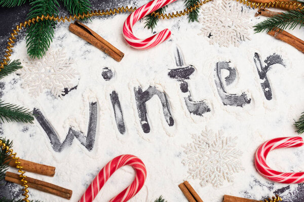 top view of word winter, fir branches and candy canes on black background