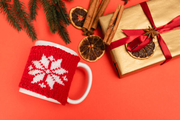top view of Christmas tree, gift with spices and mug on red background