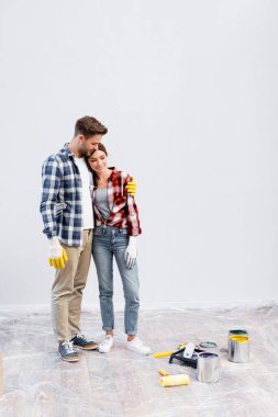 Tam boy gülümseyen genç çift evde boya kutularının, bigudilerin ve tepsilerin yanında sarılıyorlar.