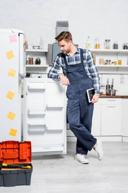 Mutfaktaki buzdolabına bakan tabletli genç bir tamirci.