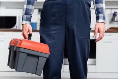 cropped view of young repairman holding toolbox with blurred kitchen on background clipart
