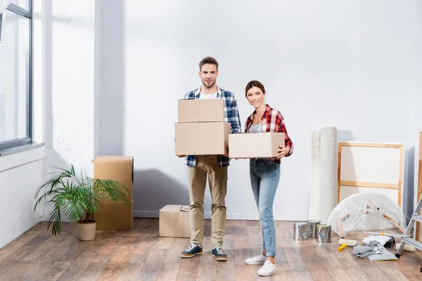 Sonriente Joven Pareja Mirando Cámara Mientras Sostiene Cajas Cartón Durante — Foto de Stock