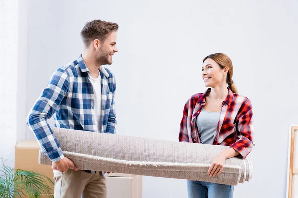 Happy Young Couple Looking Each Other While Holding Carpet Roll — Stock Photo, Image