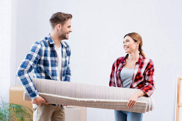 happy young couple looking at each other while holding carpet roll at home