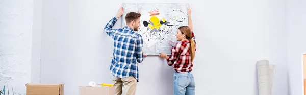 Sorrindo Jovem Casal Olhando Para Outro Enquanto Removendo Foto Casa — Fotografia de Stock