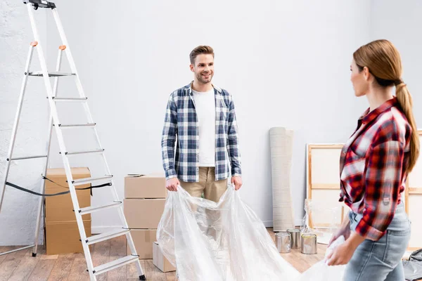 Smiling Young Man Looking Woman While Covering Room Polyethylene Repair — Stock Photo, Image