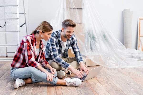 Sorrindo Jovem Casal Olhando Para Laptop Enquanto Sentado Chão Durante — Fotografia de Stock