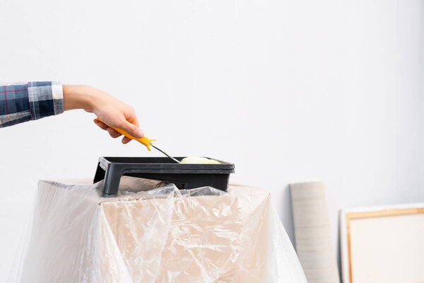 обрезанный вид человека положить краски ролика в лоток на коробке покрыты полиэтиленом на размытом фоне в помещении