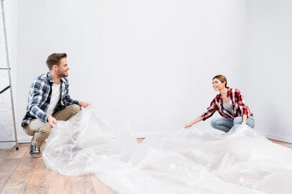 Happy Young Couple Polyethylene Covering Room While Sitting Floor Home — Stock Photo, Image