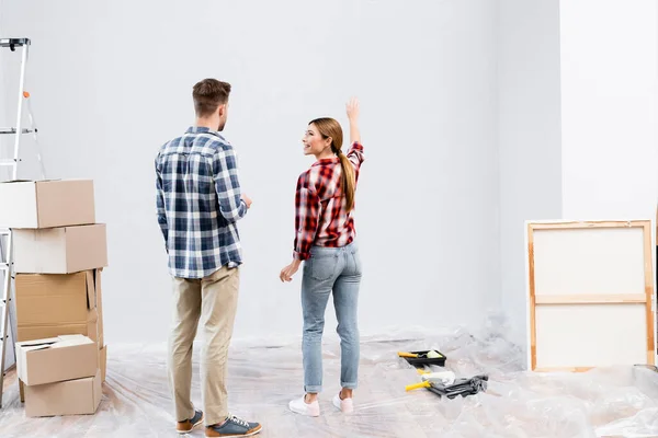 Mujer Joven Sonriente Mirando Hombre Mientras Señala Con Mano Pared — Foto de Stock