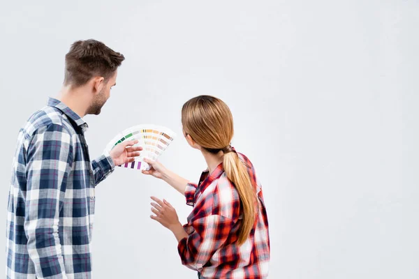 白で隔絶された壁の色を選択するパレットを持つ若いカップルのバックビュー — ストック写真