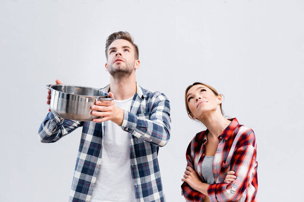 young couple holding pot while looking up under leaking ceiling 