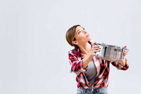 young woman looking up while holding saucepan under leaking ceiling