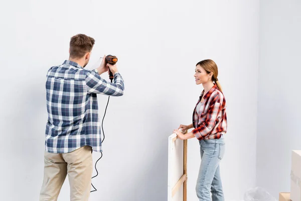 Feliz Joven Mujer Con Marco Mirando Hombre Perforación Pared Casa — Foto de Stock