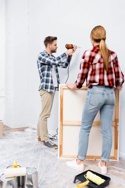 Full Length Young Woman Holding Frame Man Drilling Wall Home — Stock Photo, Image