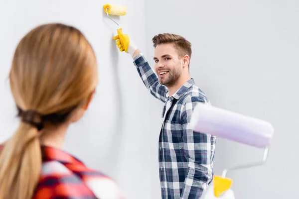Happy Young Man Roller Painting Wall While Looking Blurred Woman — Stock Photo, Image
