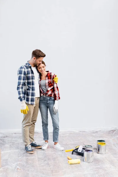 Longitud Completa Sonriente Joven Pareja Abrazándose Cerca Latas Pintura Rodillos — Foto de Stock