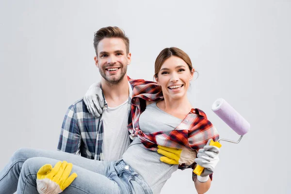 Feliz Joven Mirando Cámara Mientras Levanta Mujer Con Rodillo Pintura — Foto de Stock