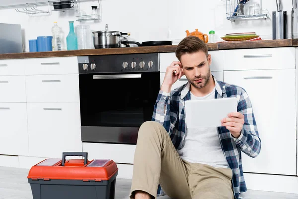 Pensive Young Man Looking Tablet While Sitting Oven Toolbox Floor — Stock Photo, Image
