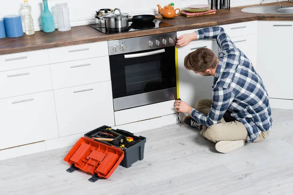 Full Length Young Man Tape Measuring Oven While Sitting Floor — Stock Photo, Image