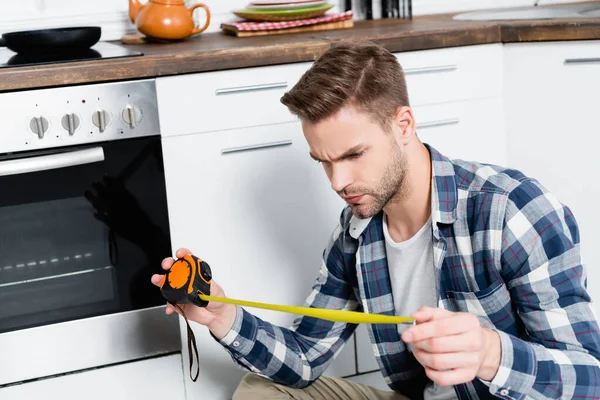 Seriös Ung Man Tittar Tejp Mått Nära Ugn Köket — Stockfoto