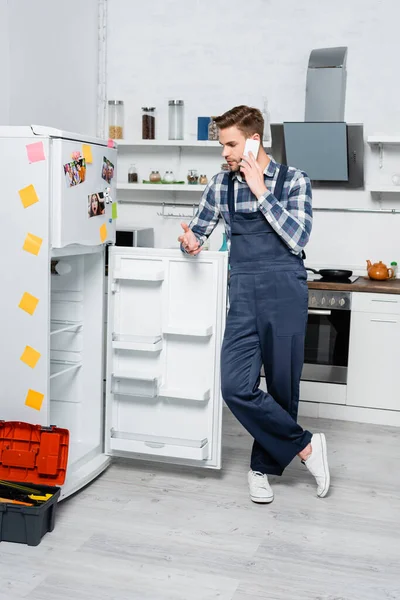 Full Length Young Repairman Talking Smartphone While Leaning Fridge Toolbox — Stock Photo, Image