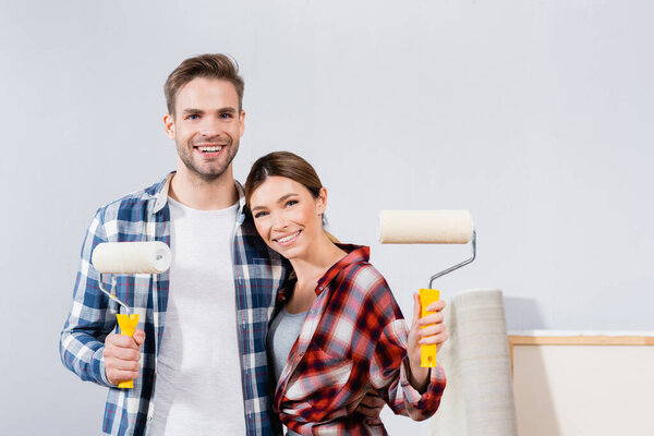 front view of happy young couple with paint rollers looking at camera while hugging at home