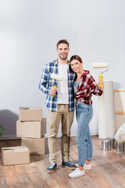 Comprimento Total Abraço Feliz Jovem Casal Enquanto Segurando Rolos Pintura — Fotografia de Stock